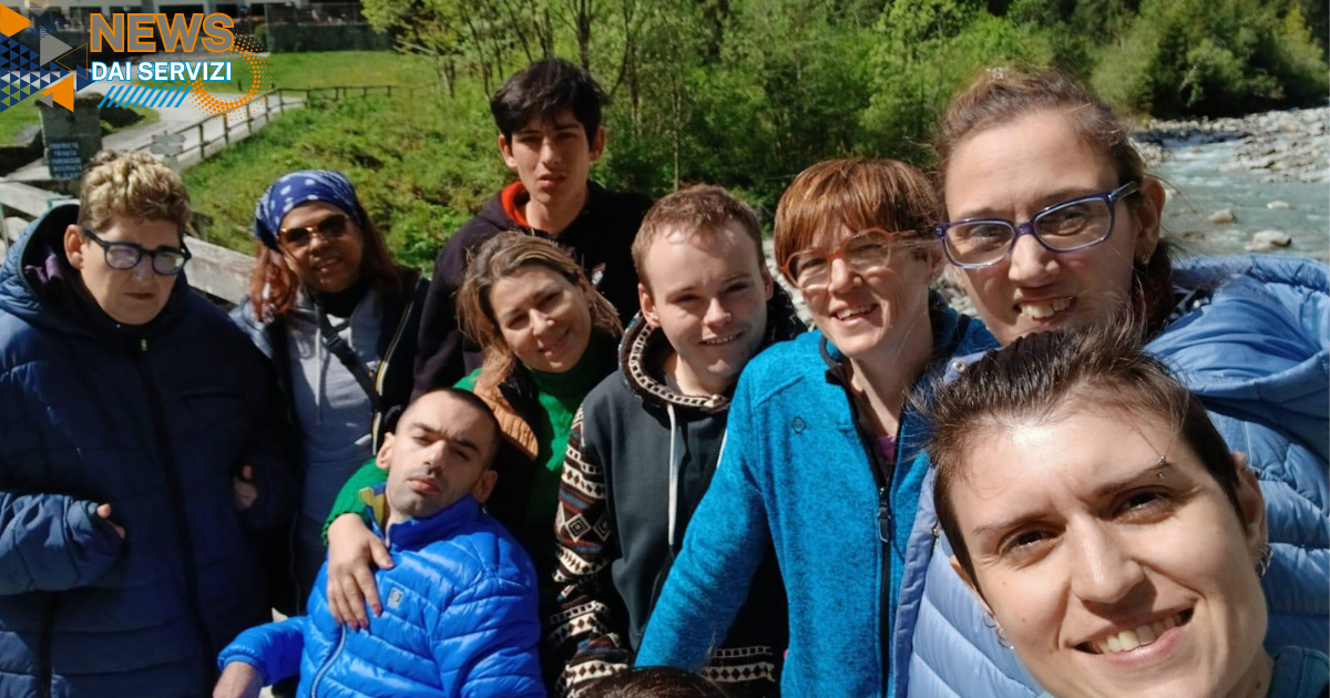 Partecipanti e operatori del Centro Socio Riabilitativo Diurno di Podenzano sorridono insieme durante il soggiorno a Carisolo, in un paesaggio naturale tra boschi, montagne e il torrente